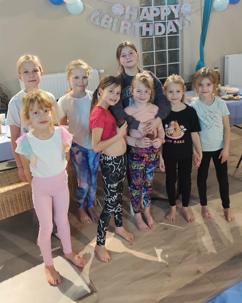 Grupa dzieci na urodzinach w sali AerialParadise, w tle girlanda „Happy Birthday” i szarfa